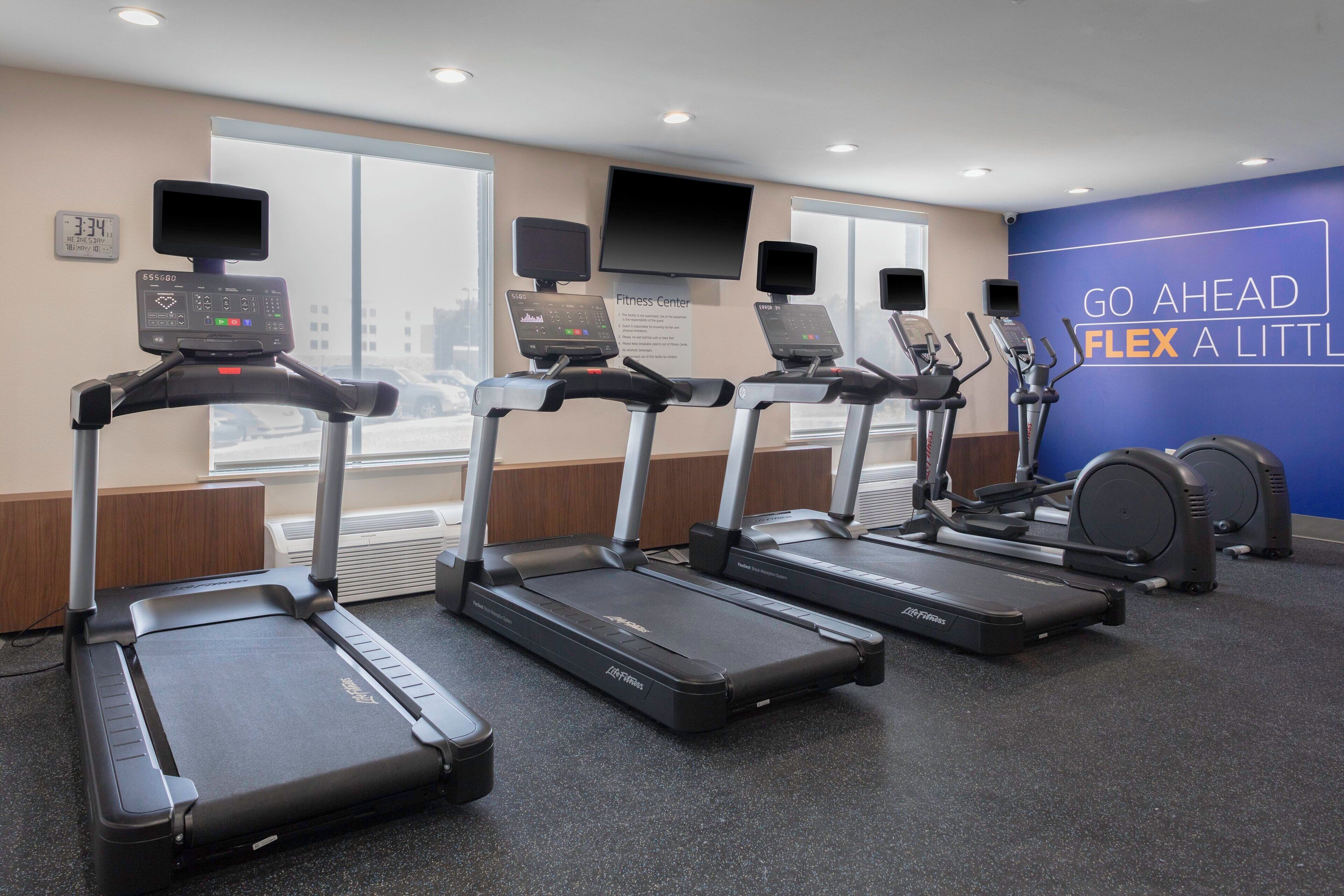 A fitness center with treadmills, a stationary bike, and a wall with motivational text.