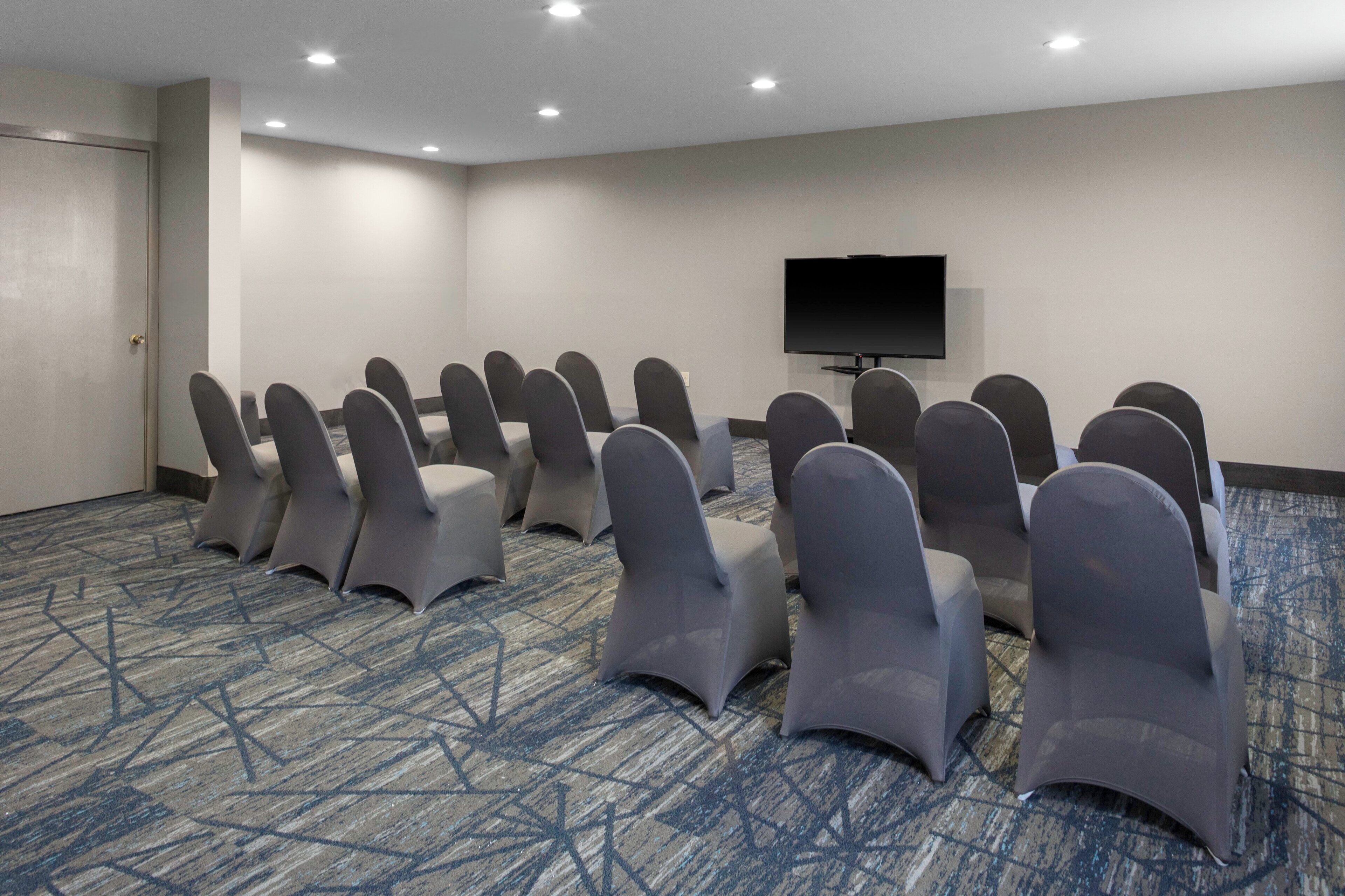 A conference room with rows of chairs and a flat-screen TV on the wall.