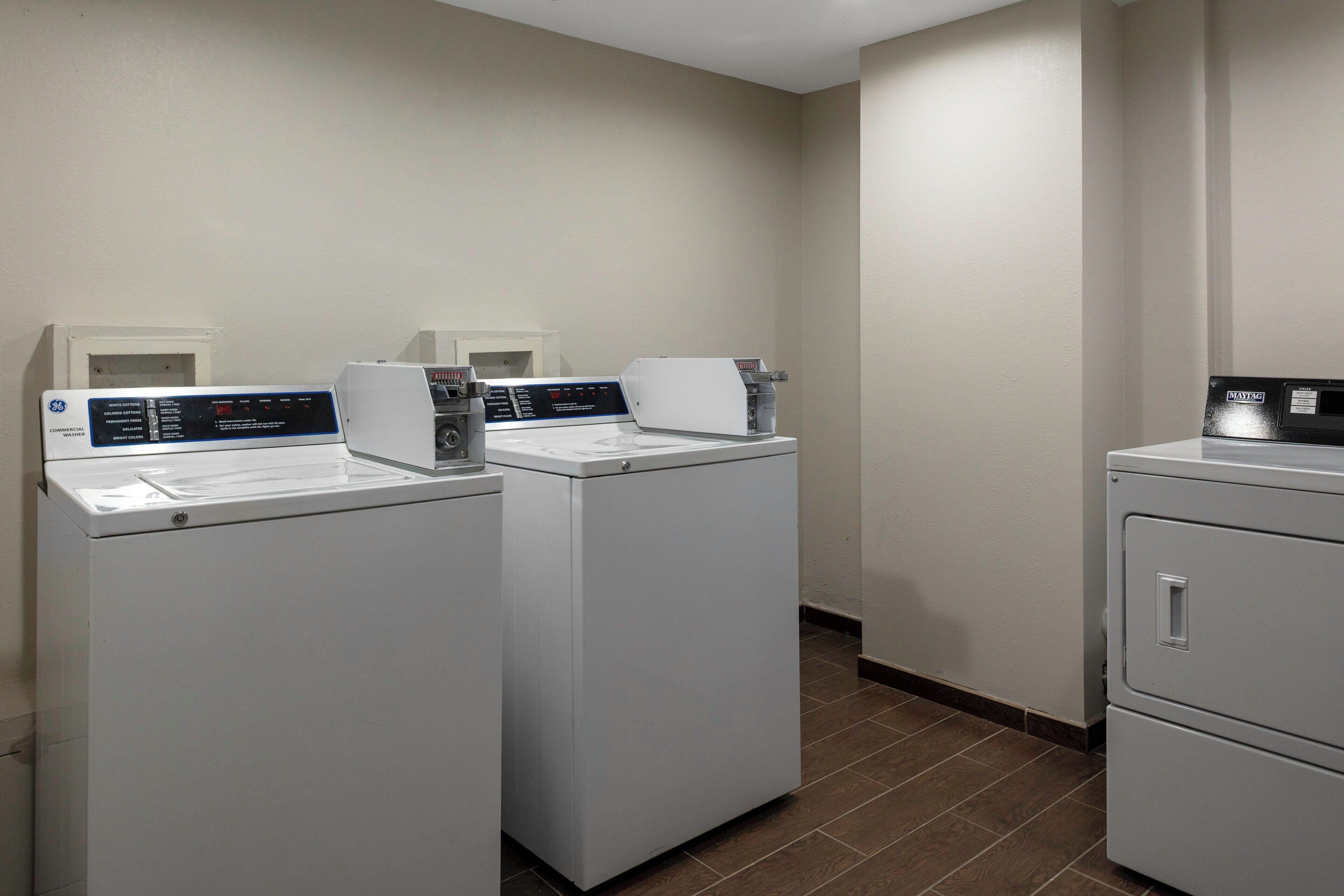 Un lavadero con dos lavadoras de carga frontal y una secadora.