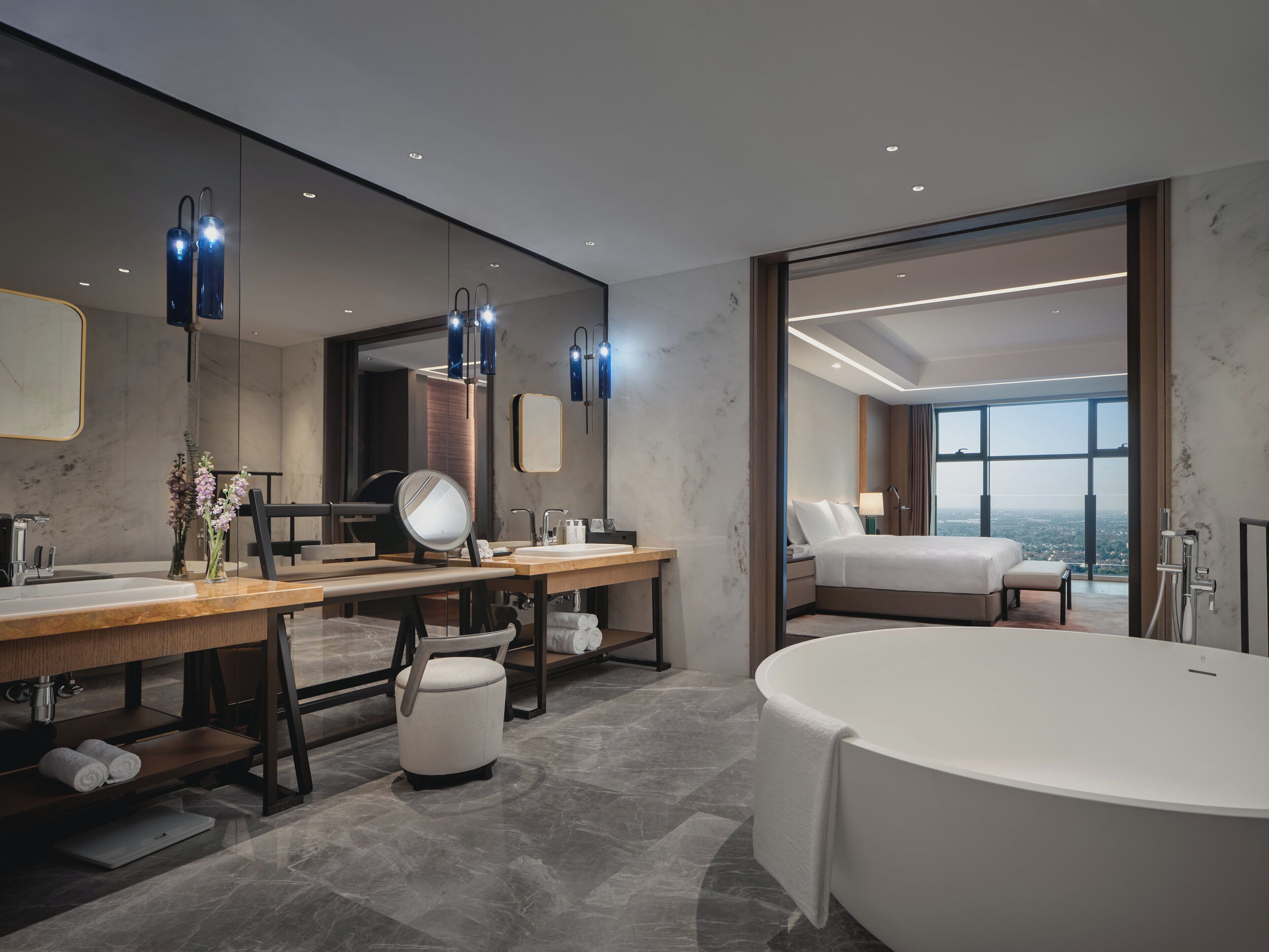 A modern bathroom with a large bathtub, a vanity with a mirror, and a large window offering a city view.