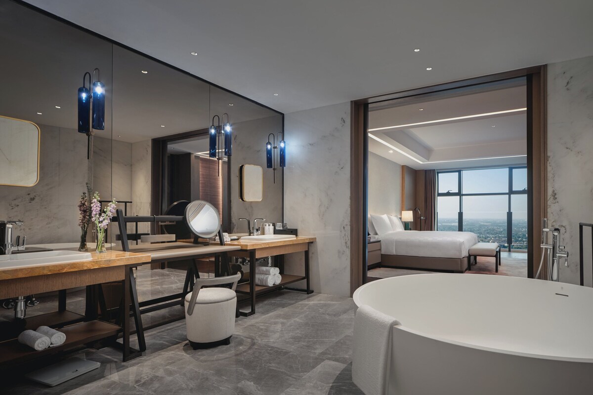 Un baño moderno con una bañera grande, un tocador con espejo y un ventanal con vistas a la ciudad.