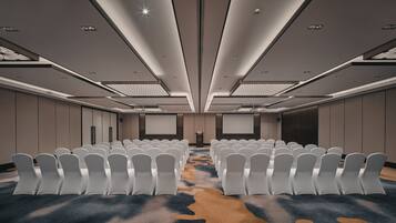 A conference room with rows of white chairs, a large screen, and a podium.