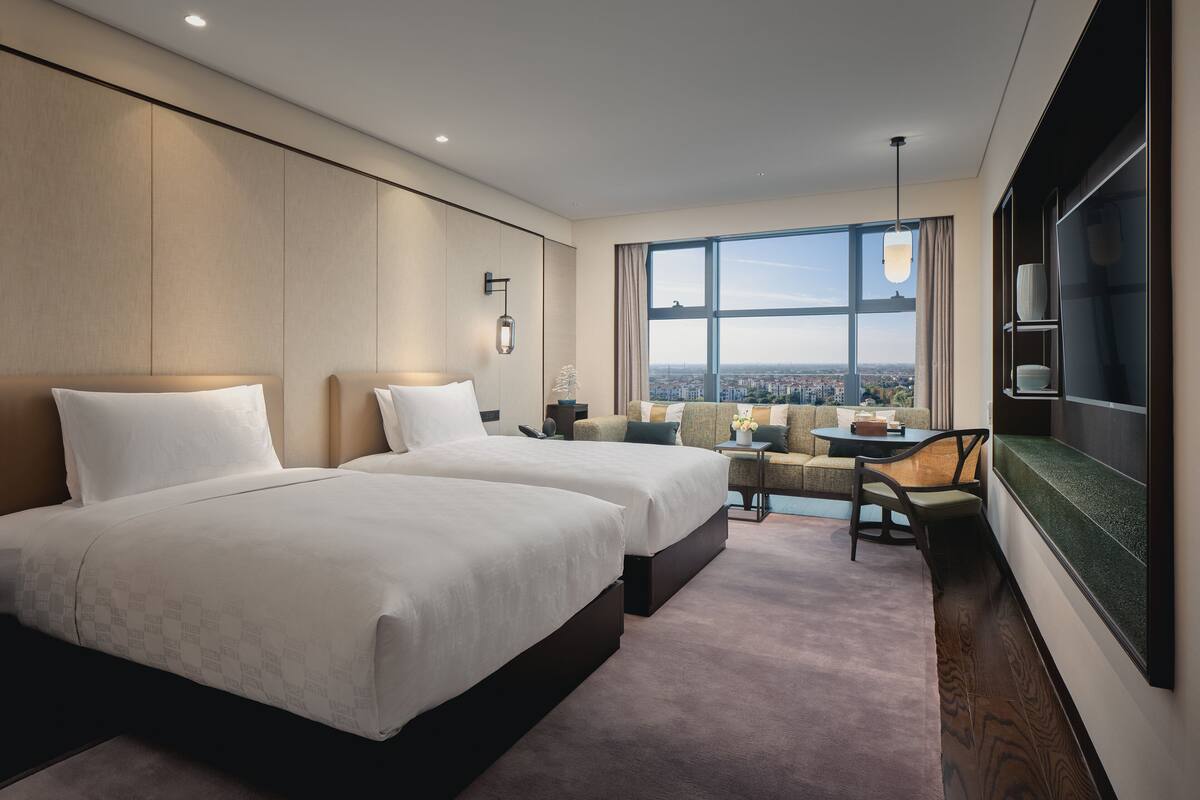 Camera d'albergo con due letti, una poltrona letto, un tavolo da pranzo e un'ampia finestra con vista sulla città.