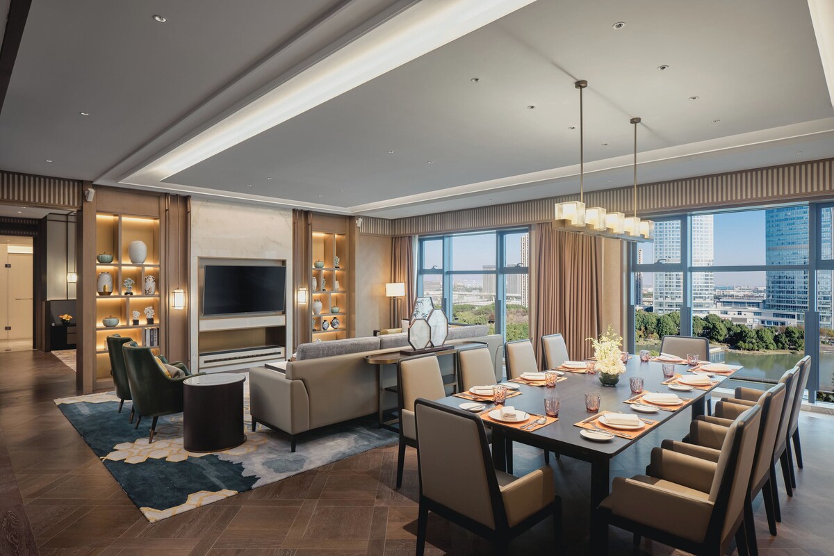 Una habitación de hotel moderna con zona de comedor, sofá, televisor y vistas de la ciudad.
