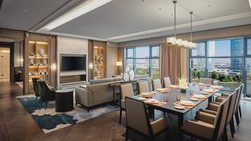 Una habitación de hotel moderna con zona de comedor, sofá, televisor y vistas de la ciudad.