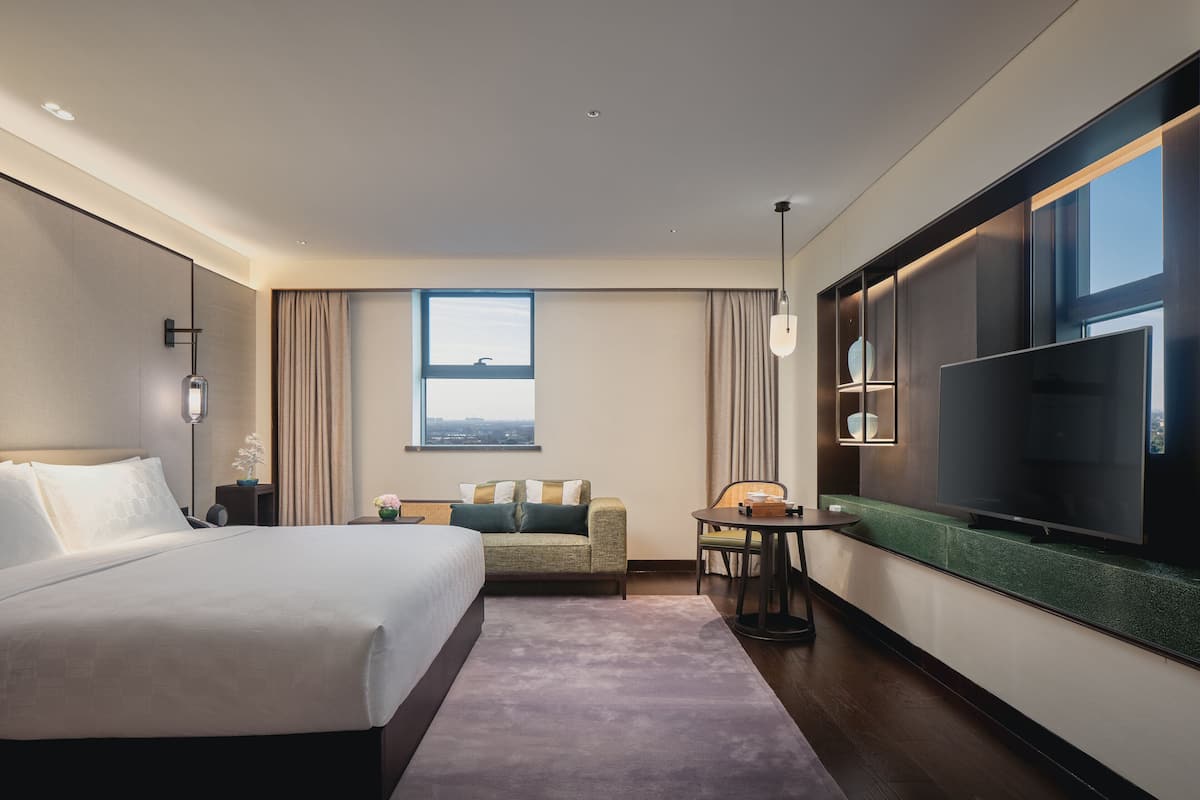 Una moderna camera d'albergo con un letto grande, un divano, un tavolino, una TV e una finestra con vista sulla città.