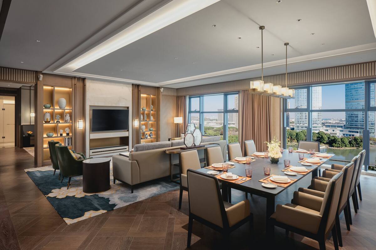 Una moderna camera d'albergo con zona pranzo, divano, TV e vista sulla città.