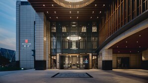 A modern hotel entrance with a curved light fixture above the doors, large windows, and a sign reading "HUALUX". - HUALUXE Kunshan Huaqiao by IHG (Suzhou)