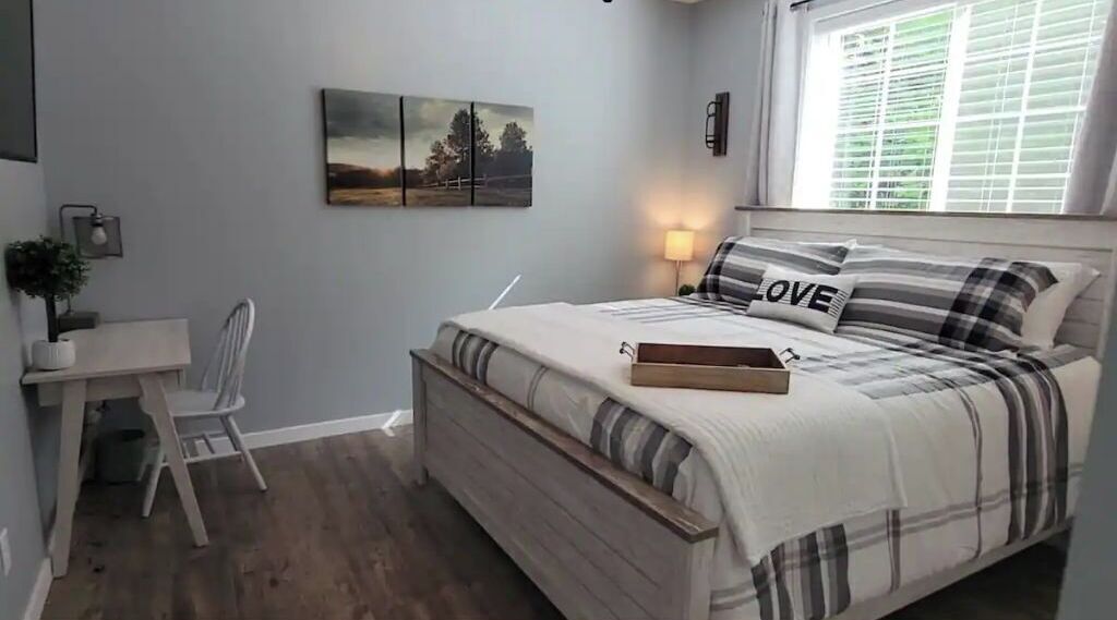 A bedroom with a bed, bedside table, lamp, and a painting on the wall.