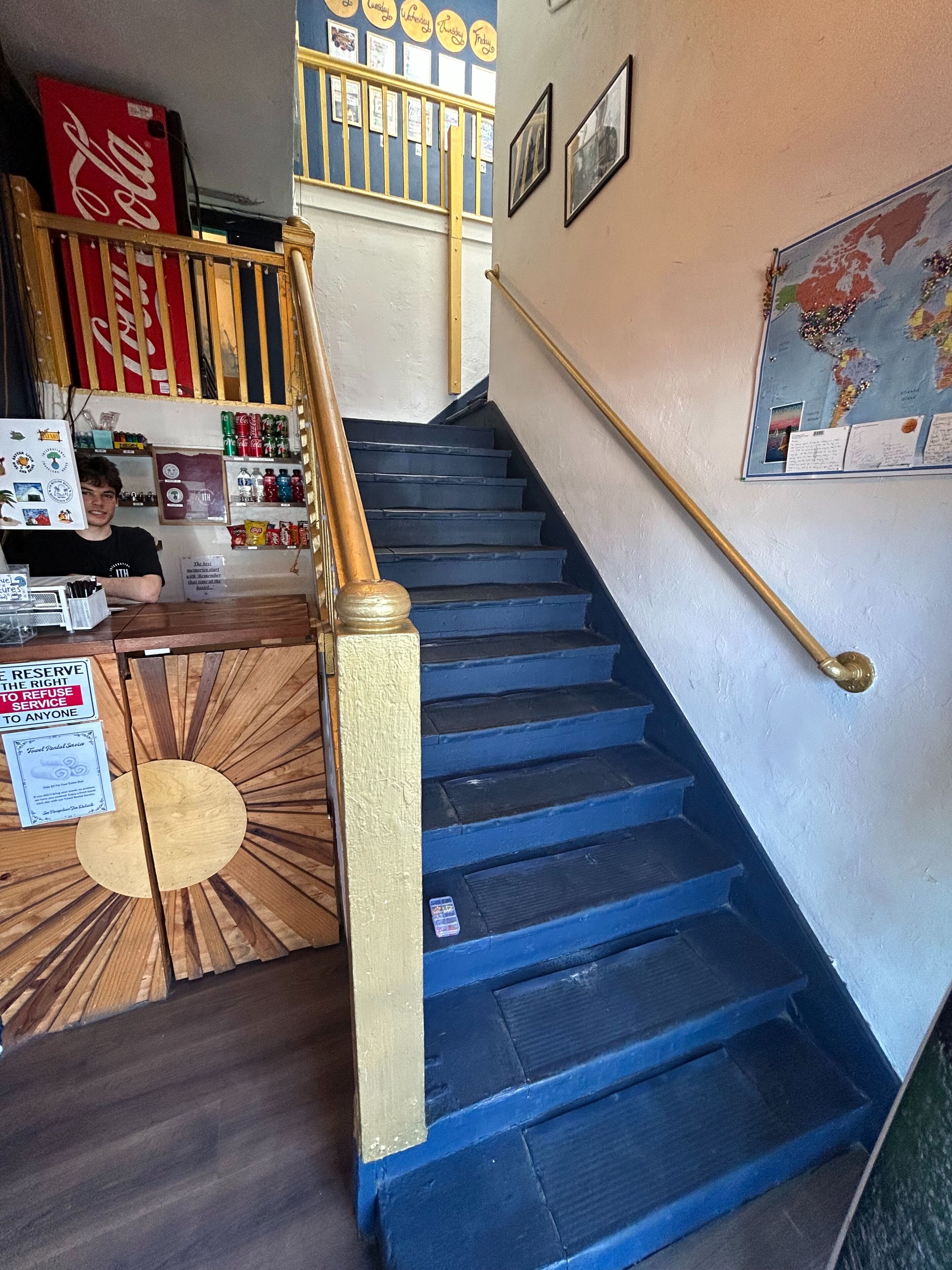 A staircase with blue steps, a wooden handrail, and a wall with a map and framed pictures.