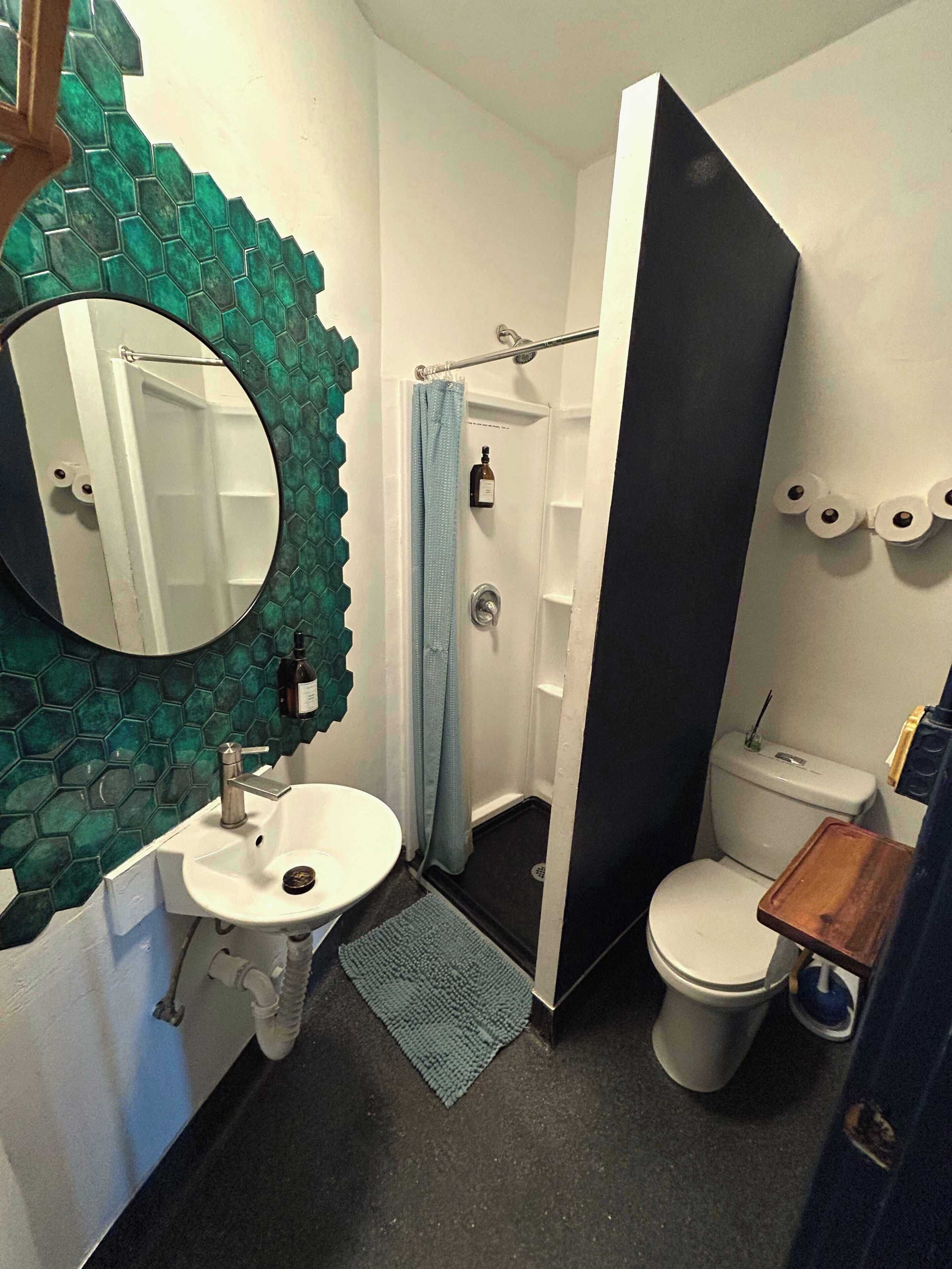 A bathroom with a round mirror, a sink, a toilet, and a shower area.