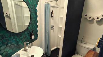 A bathroom with a round mirror, a sink, a toilet, and a shower area.