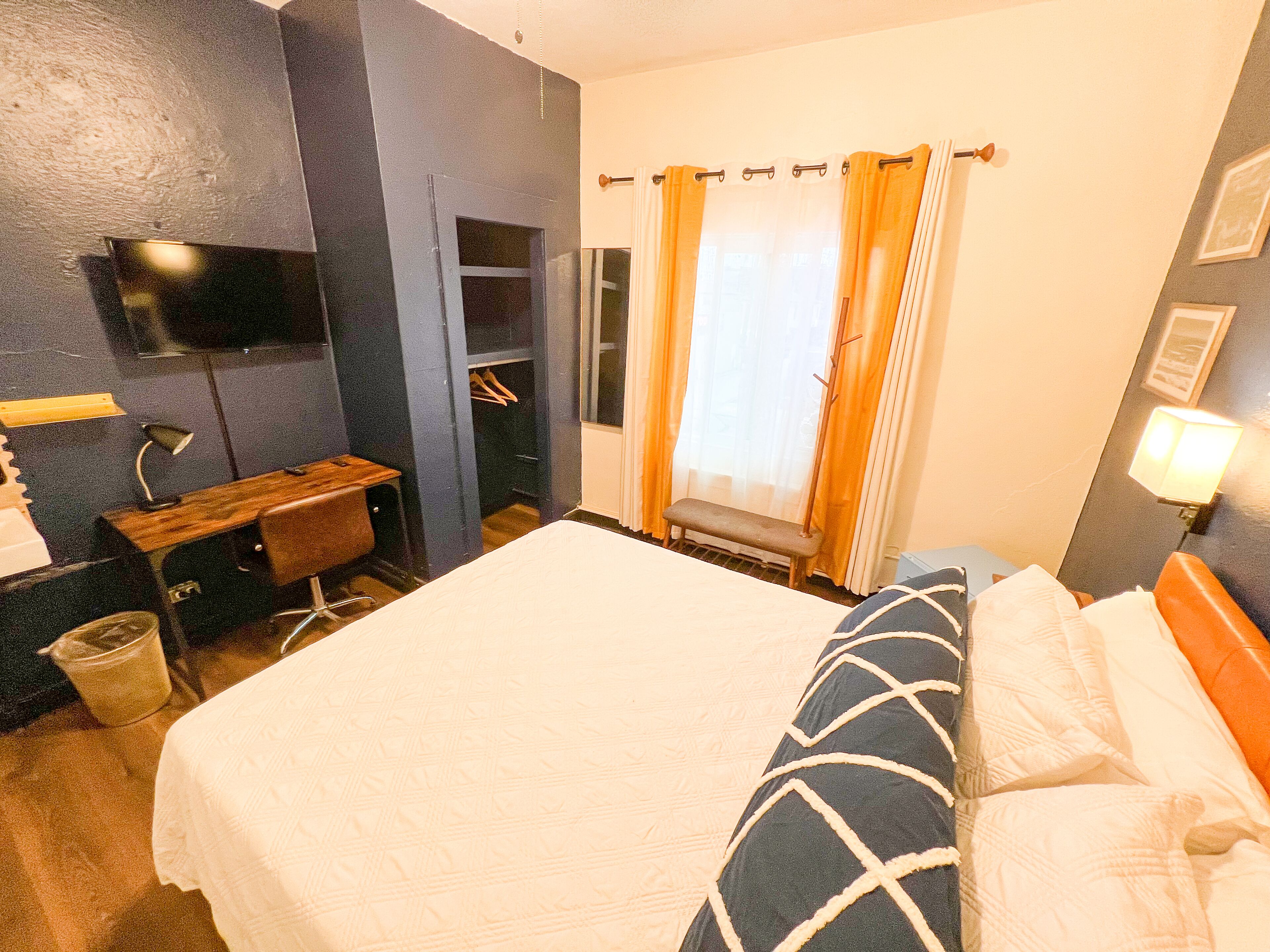 Habitación de hotel con cama, escritorio, silla, televisor y ventana con cortinas.