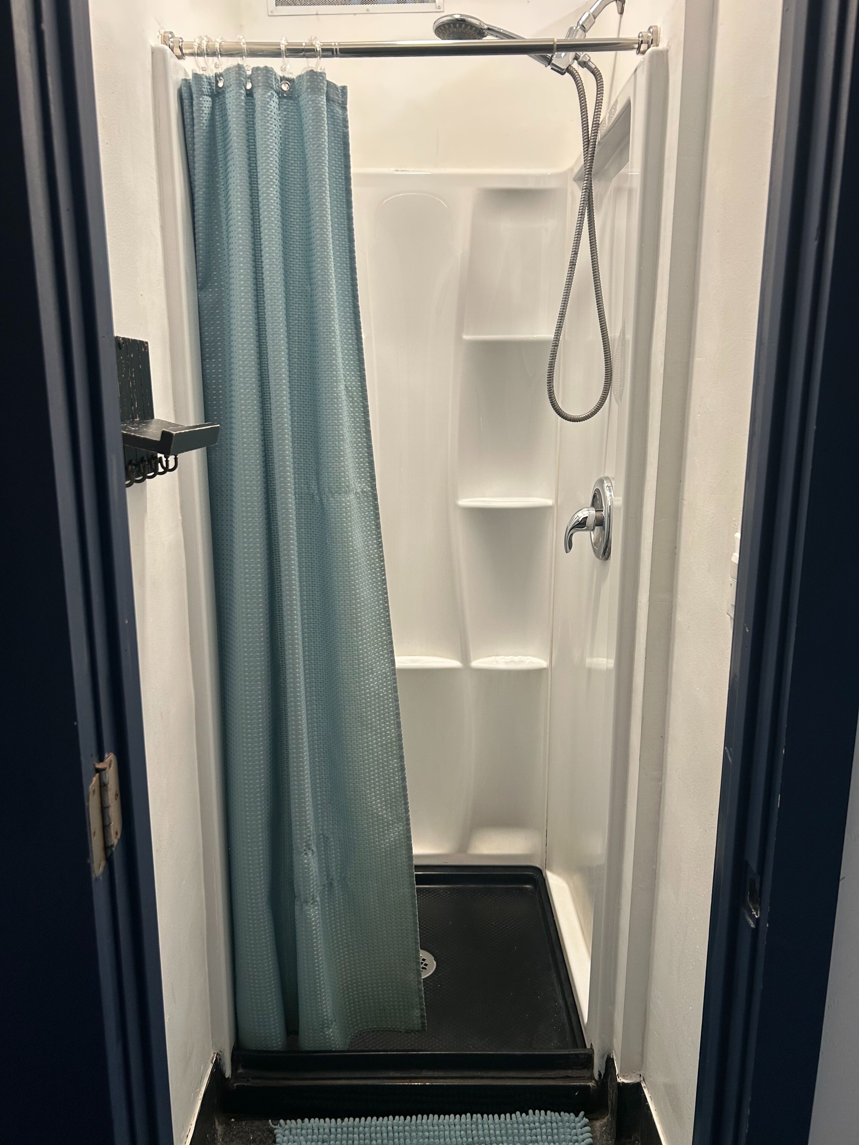 A shower with a blue shower curtain, a handheld showerhead, and a wall-mounted faucet.