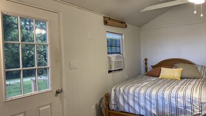 Un dormitorio con cama, ventana, equipo de aire acondicionado y ventilador de techo.