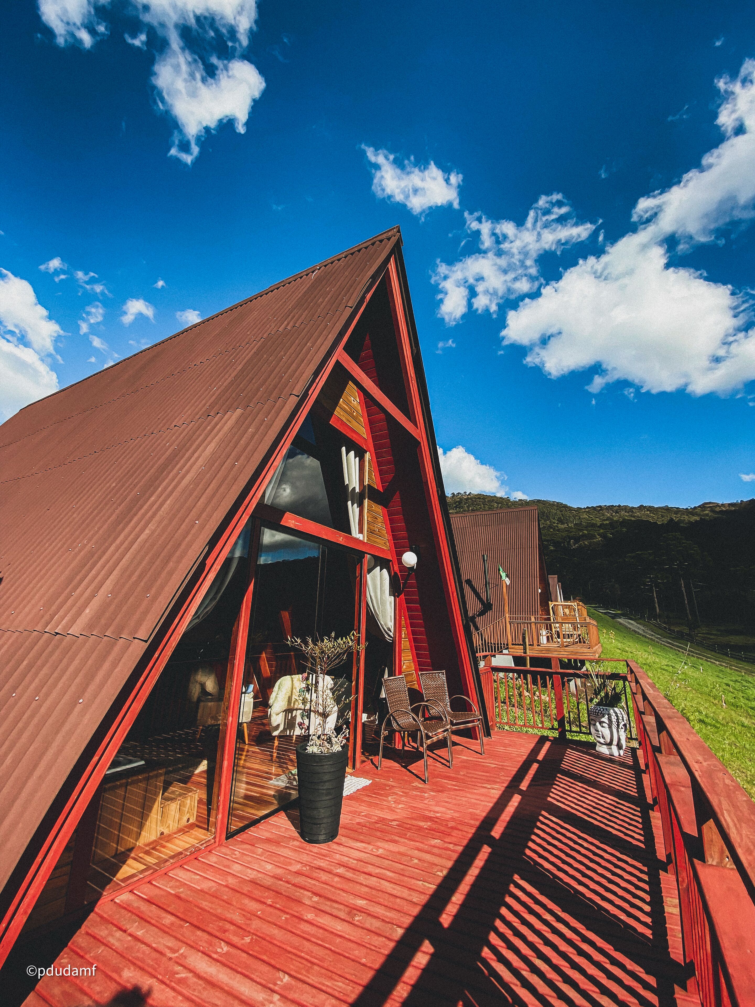 A red-roofed building with a wooden deck, a large window, and a view of the surrounding landscape.