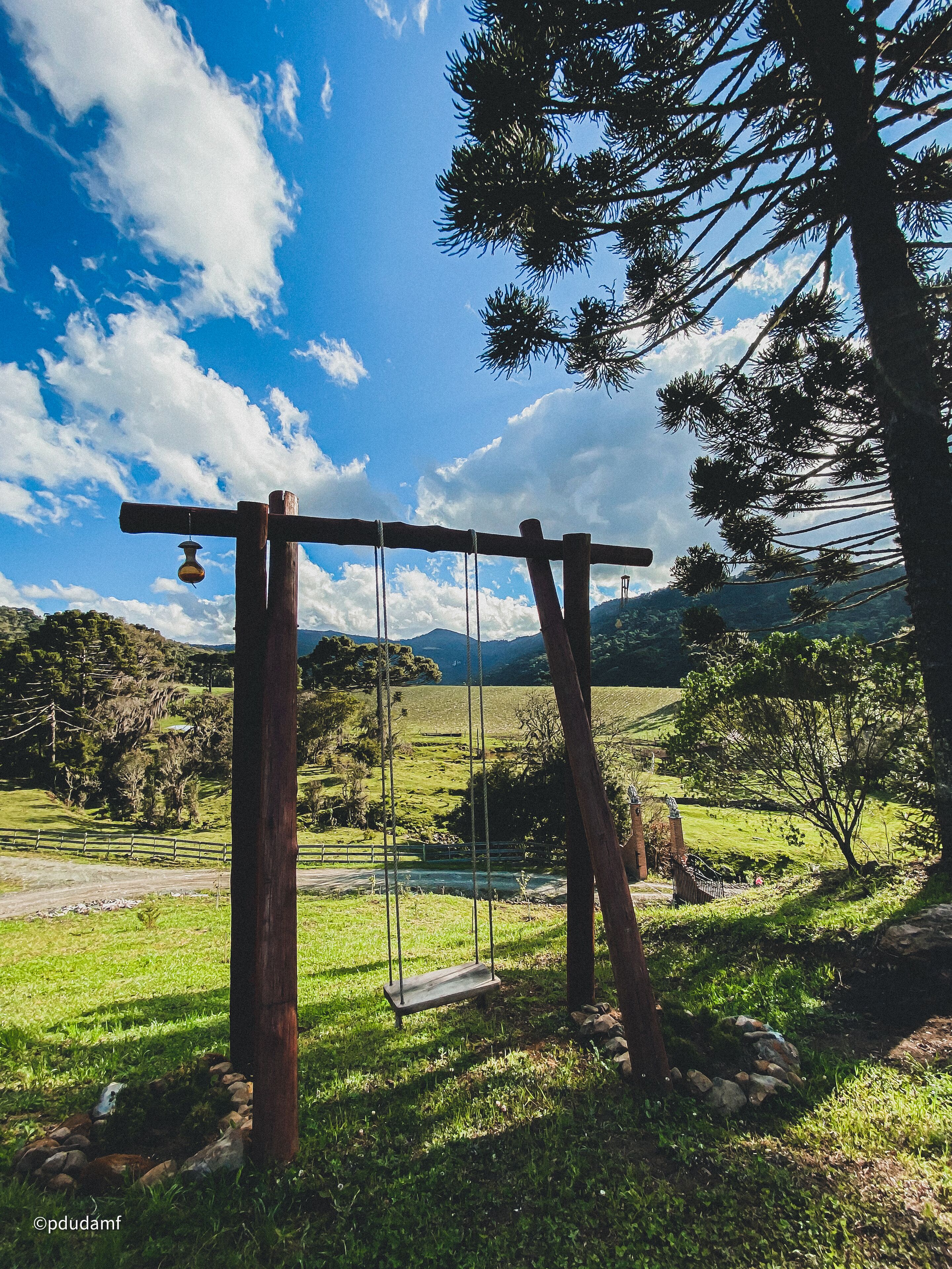 A wooden swing set in a grassy field with a clear sky and distant mountains.