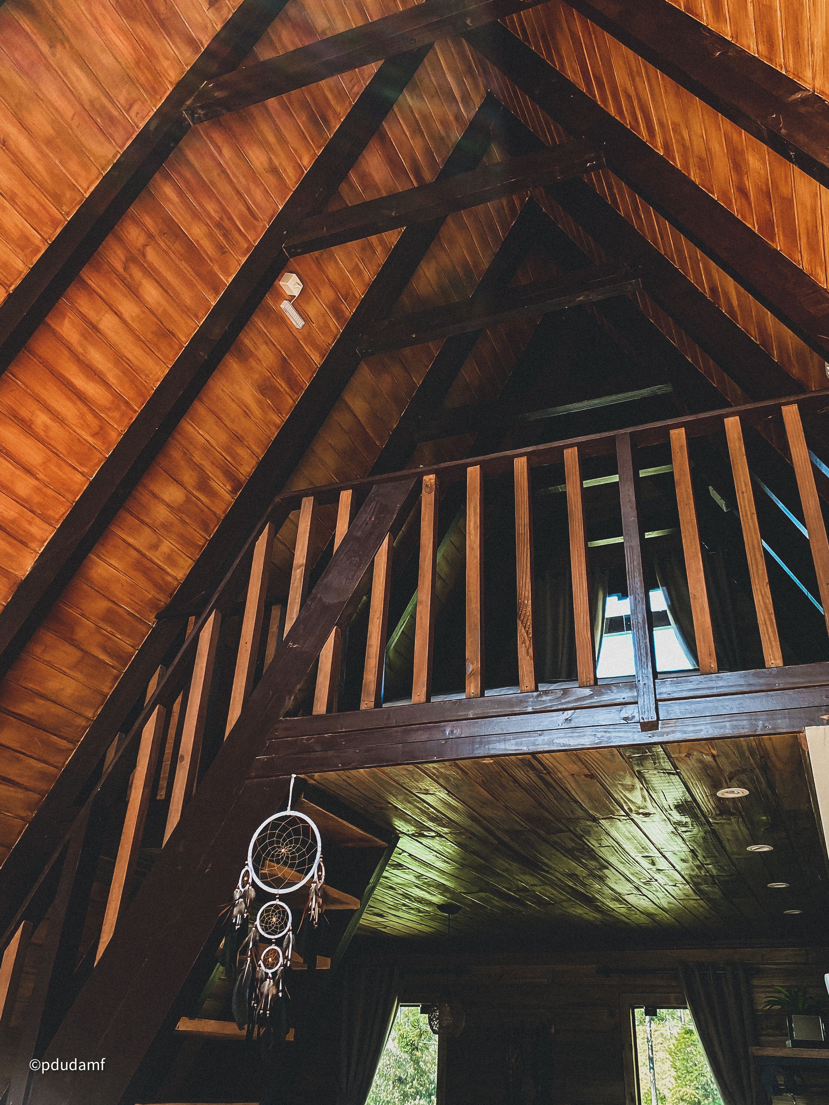 A wooden ceiling with exposed beams and a dreamcatcher hanging from the ceiling.