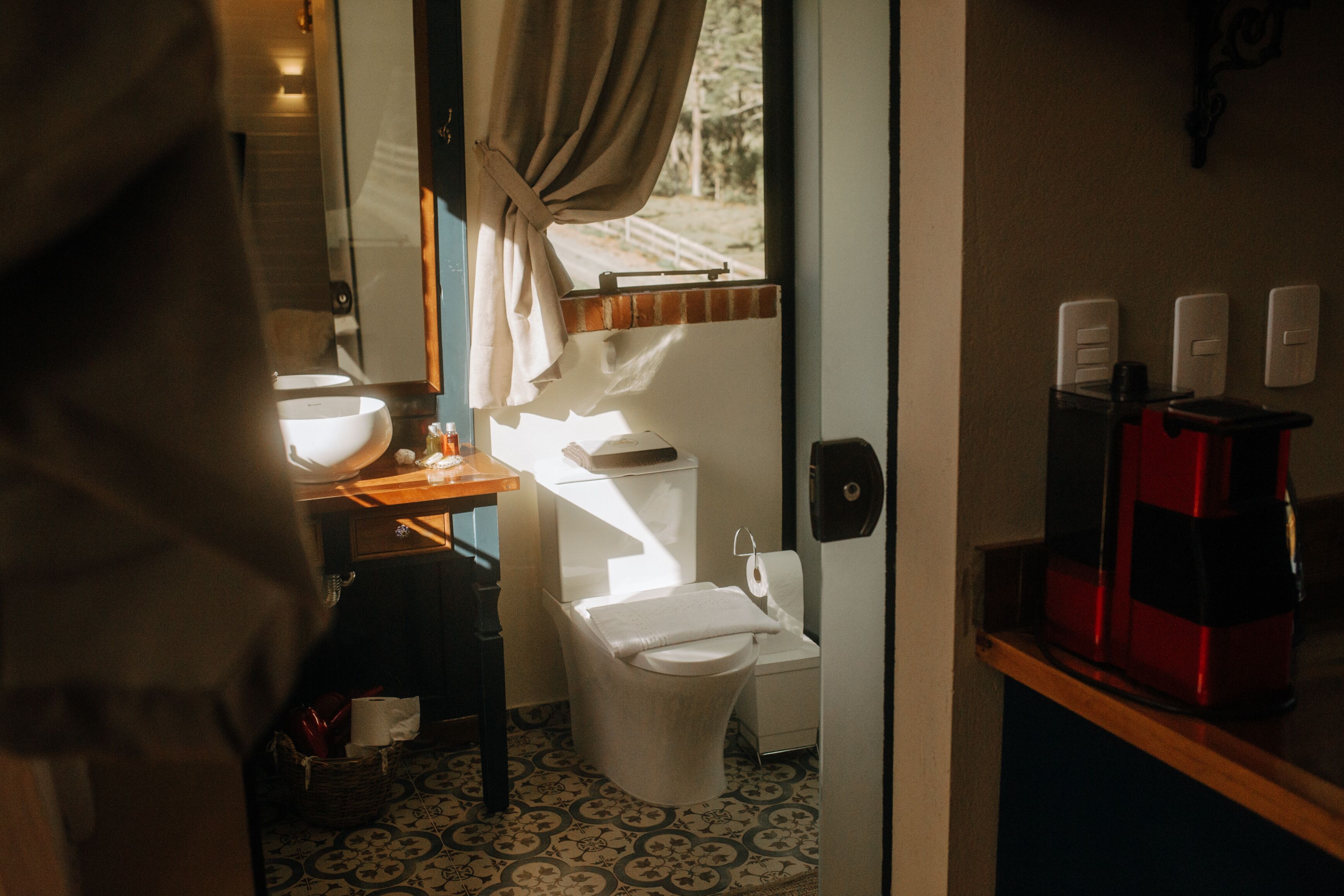 A compact bathroom with a toilet, sink, and a coffee machine on a shelf.