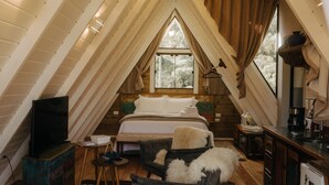 A cozy attic bedroom with a large bed, a television, a chair, and a small table. - Estância Nazari (Urubici)