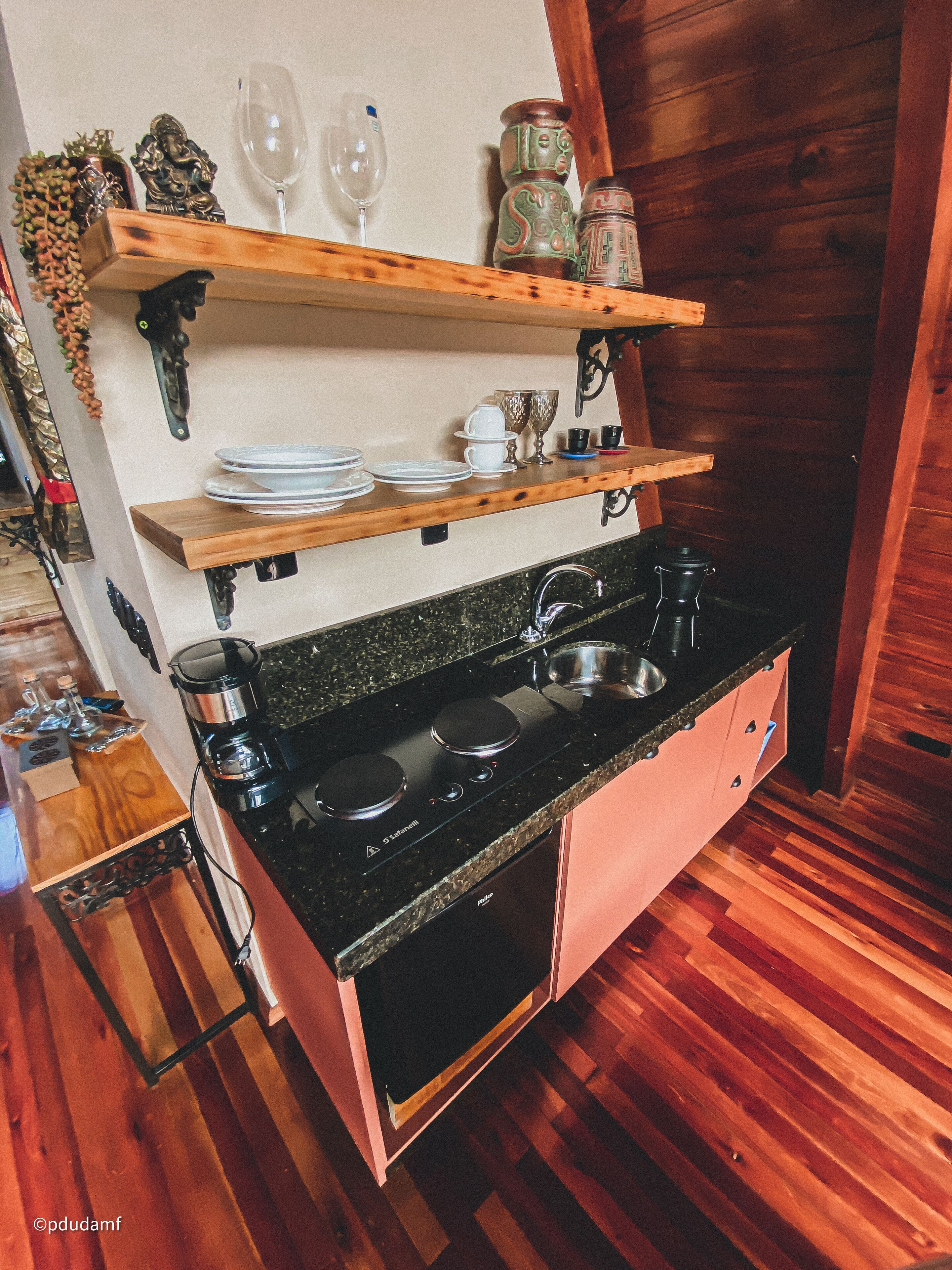 A compact kitchen with a black stove, wooden shelves, and a wooden floor.