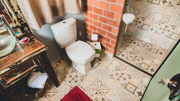 Ein Badezimmer mit Toilette, Waschbecken und Spiegel an einer Ziegelwand. Der Boden ist mit einem Muster versehen und ein roter Teppich liegt darauf.