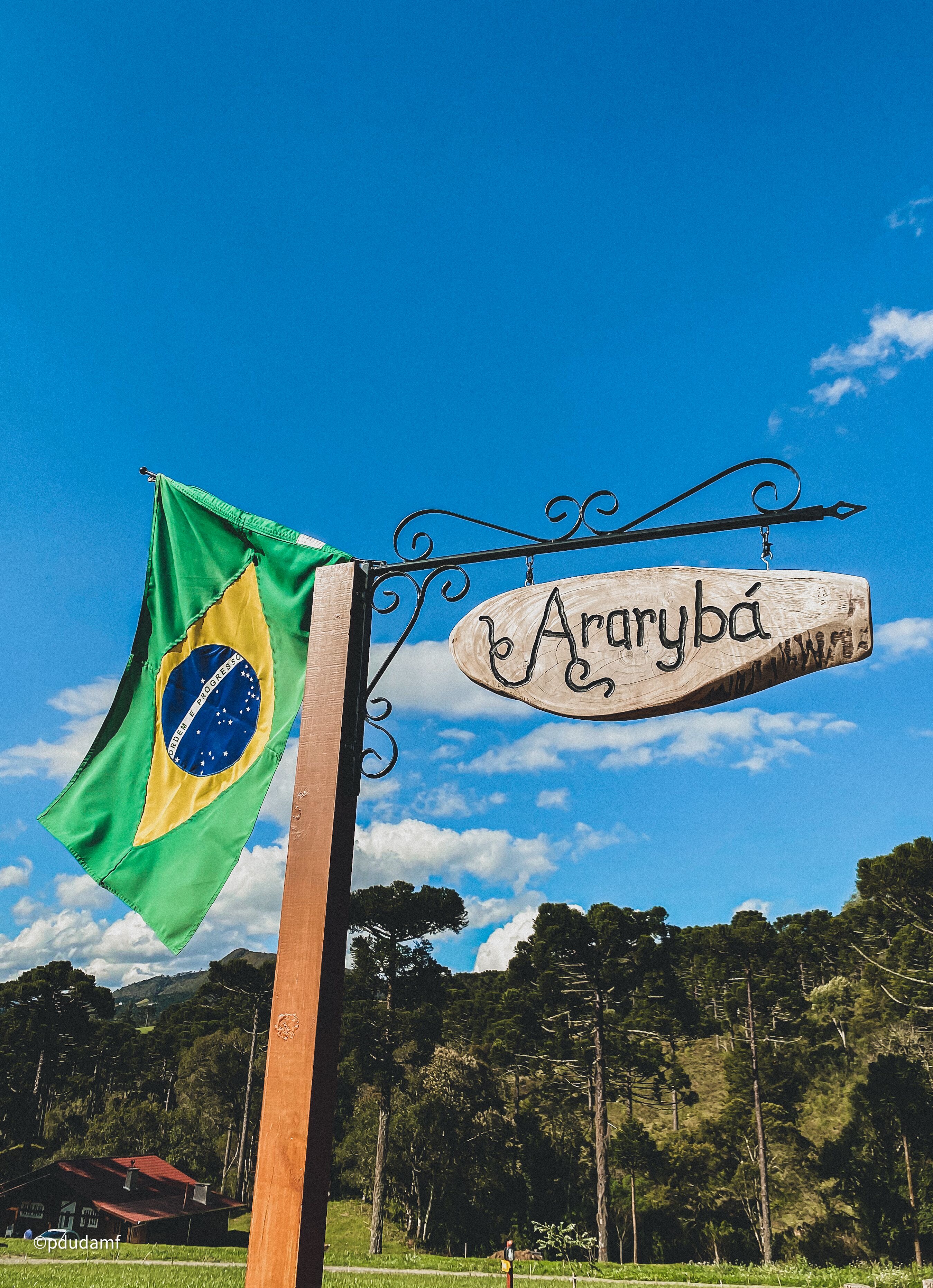 A wooden sign with the name 'Araryba' hanging from a metal post, alongside a Brazilian flag.