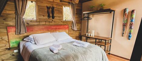 Un dormitorio de cabaña de madera con una cama, cortinas, una planta colgante y esquíes en la pared.