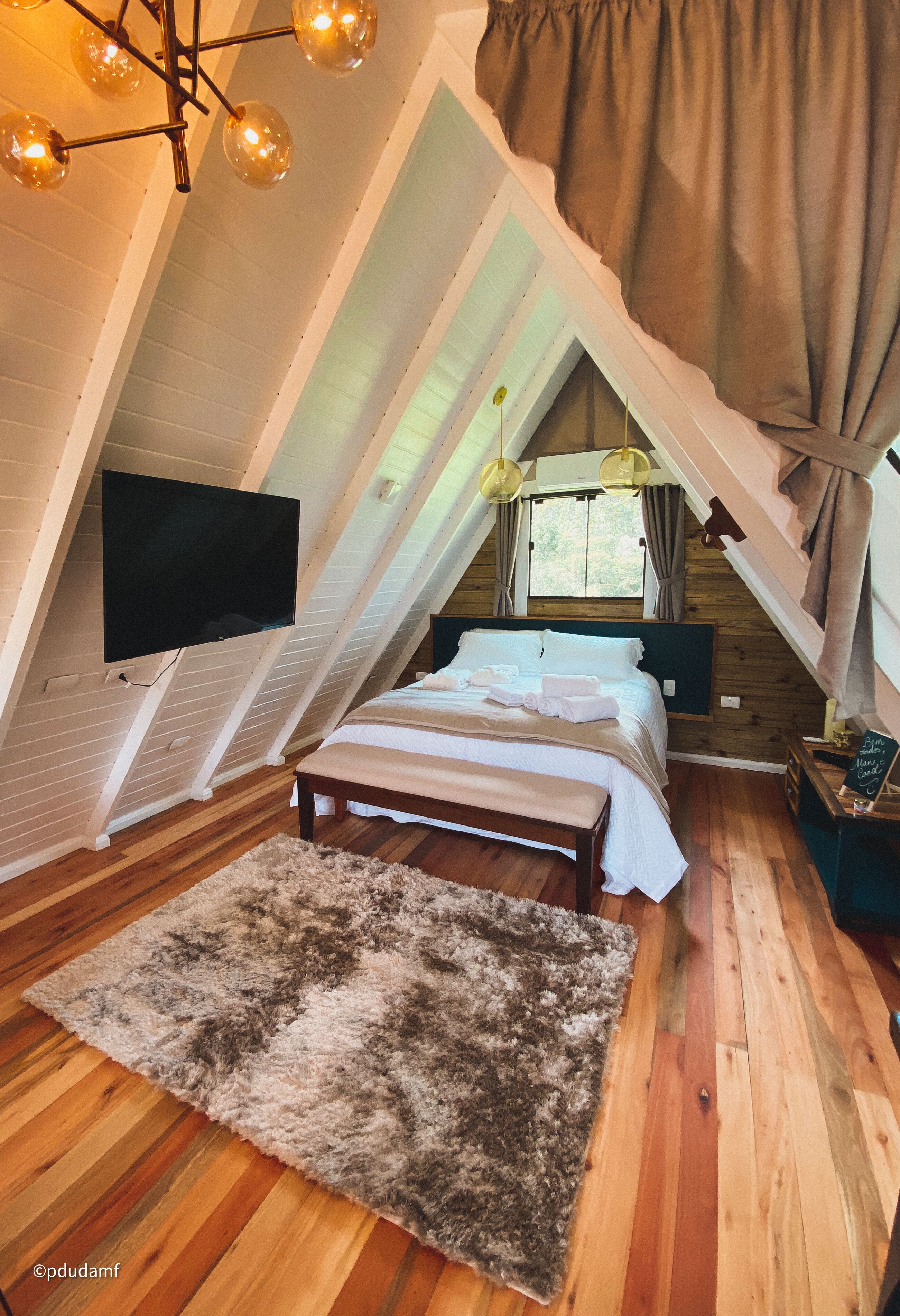 Ein gemütliches Schlafzimmer im Dachgeschoss mit Bett, Nachttisch und an der Wand montiertem Fernseher.
