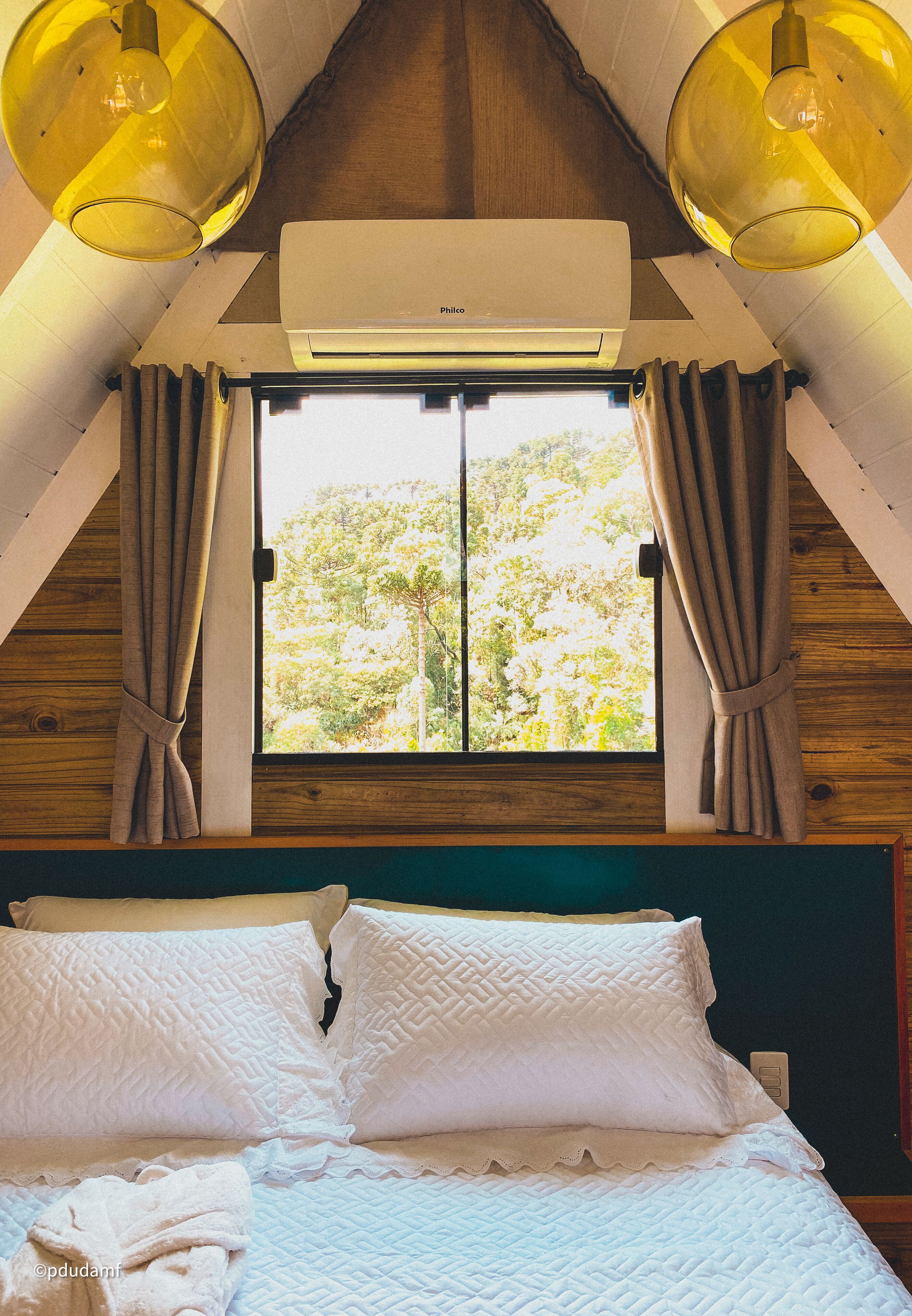 A bedroom with a large window, a bed with white bedding, and an air conditioning unit above the window.