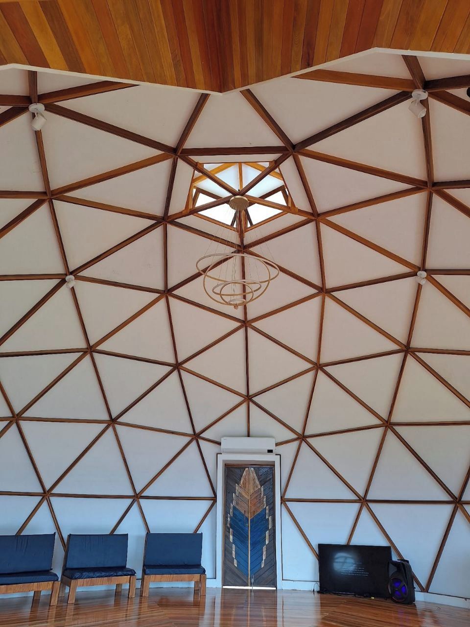 A room with a geometric ceiling design, a central door, and seating along the walls.