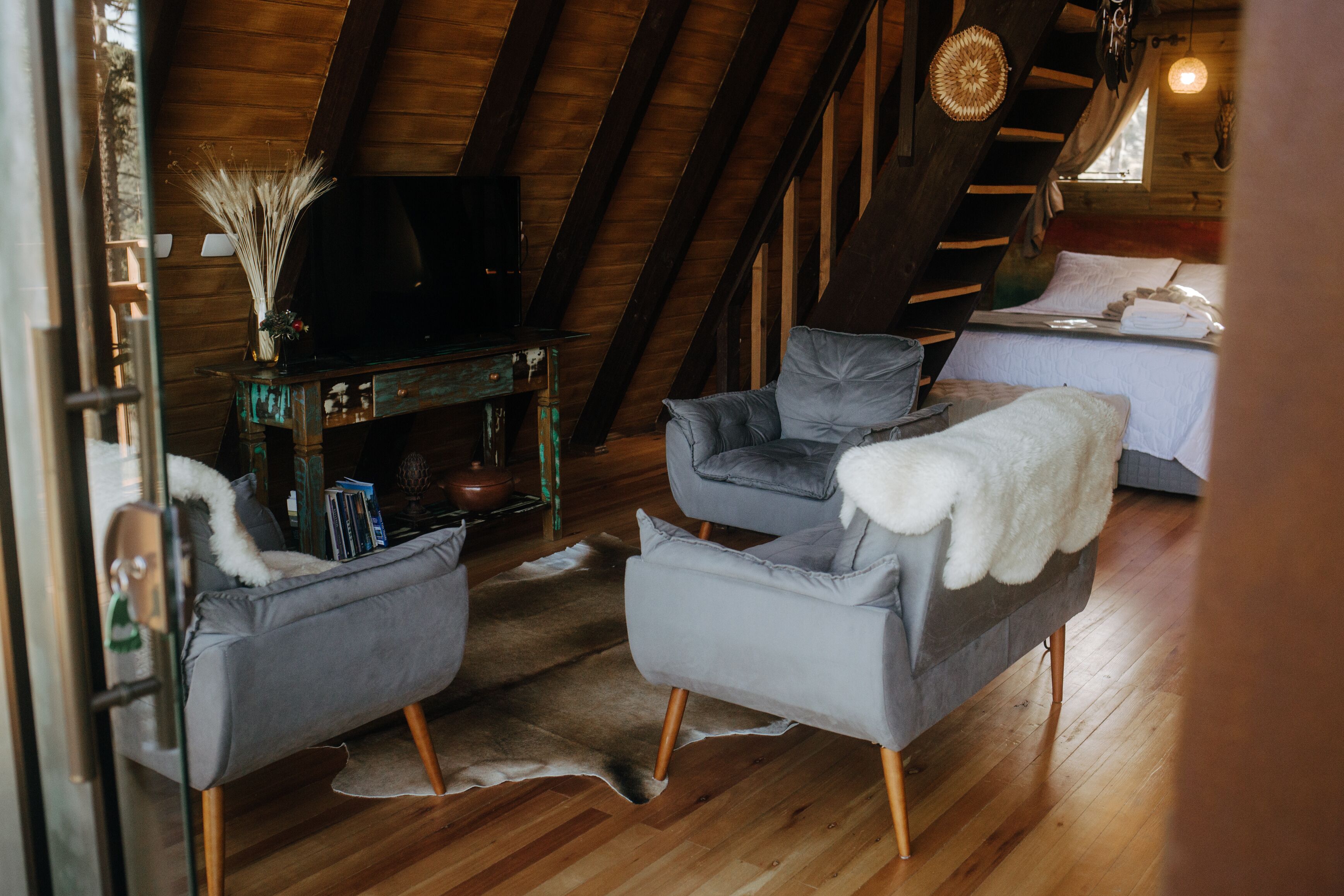 A cozy loft bedroom with a wooden ceiling, a bed with white bedding, and two grey armchairs.