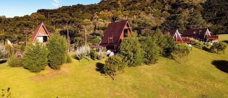 A rural setting with three cabins surrounded by lush greenery and a forested hill in the background.