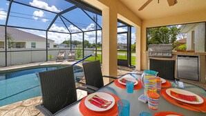 Une terrasse extérieure avec une table en verre, des chaises, une piscine et un espace barbecue.