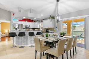 A modern kitchen with white cabinets, a central island with bar stools, and a dining area with a table set for six.
