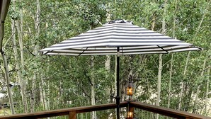 Een houten terras met lounge fauteuils, een gestreepte parasol en een tafel met stoelen.