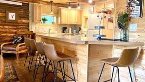 Een keuken in blokhutstijl met houten wanden, een centraal eiland met barstoelen en een bord met regels voor de blokhut.