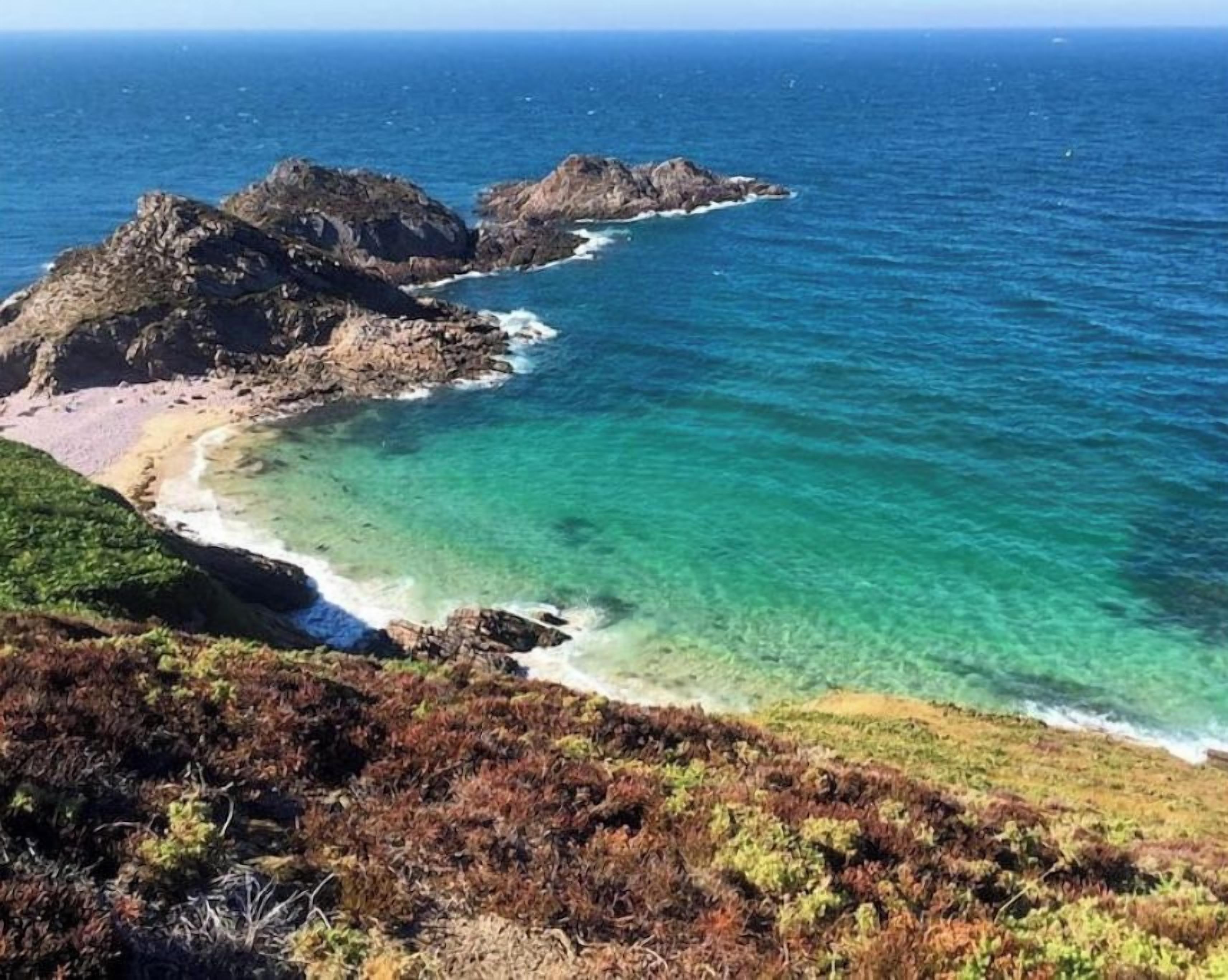 A coastal landscape with rocky outcrops and clear turquoise waters.