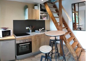 A kitchen with a wooden staircase, a microwave, a stove, and two stools.