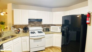 Une cuisine moderne avec des meubles blancs, une cuisinière à gaz, un four à micro-ondes et un réfrigérateur noir.