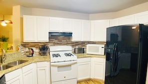 A modern kitchen with white cabinets, a gas stove, a microwave, and a black refrigerator. - Spacious 4BR with 6 Beds Sleeps 12. near I45 Round Rock (Round Rock)
