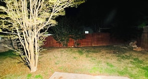 A backyard with a tree, a wooden fence, and a concrete slab. - Spacious 4BR with 6 Beds Sleeps 12. near I45 Round Rock (Round Rock)