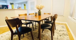 A dining room with a wooden table and six chairs, a vase with dried flowers, and a kitchen in the background. - Spacious 4BR with 6 Beds Sleeps 12. near I45 Round Rock (Round Rock)