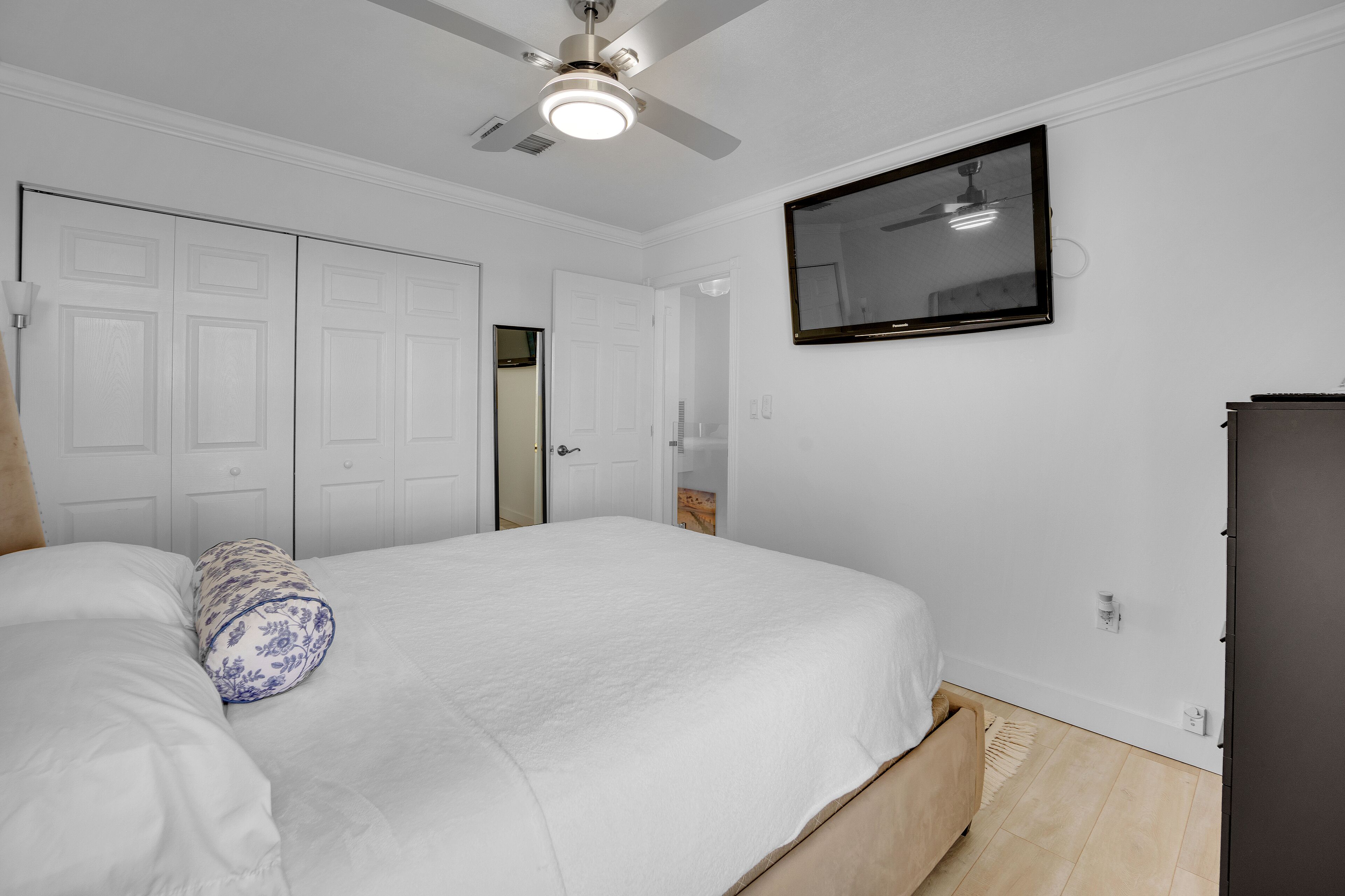 A bedroom with a bed, a ceiling fan, a television, and a wardrobe.