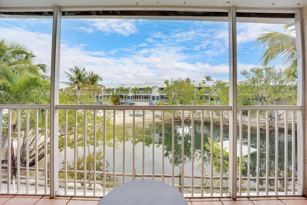 A balcony with a view of a body of water, palm trees, and a building in the background.