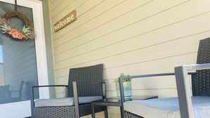 Eine Veranda mit zwei Korbstühlen, einem kleinen Tisch und einem Willkommensschild.