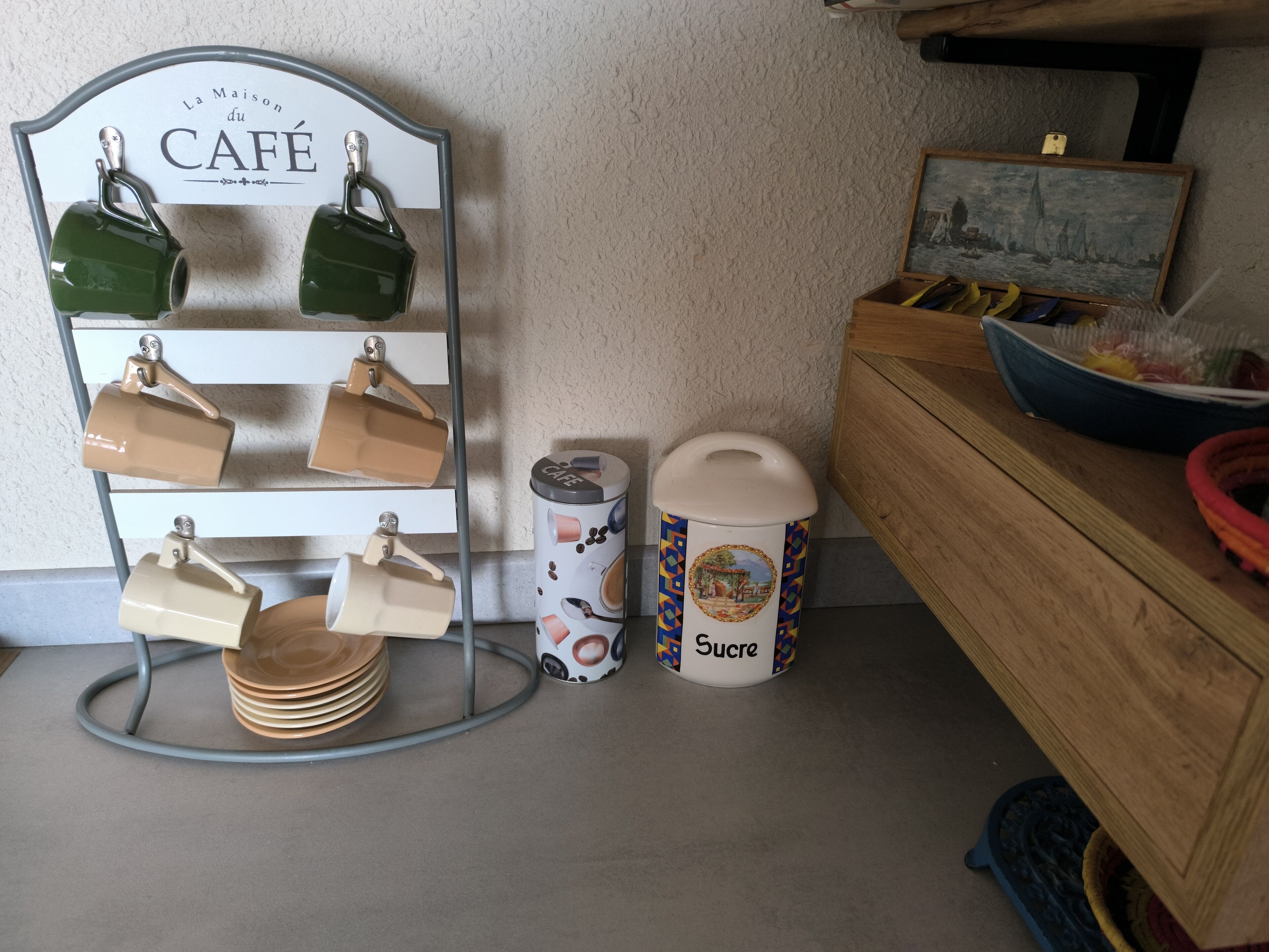 Een keukentafel met een koffiekop houder, een prullenbak en een houten kast.