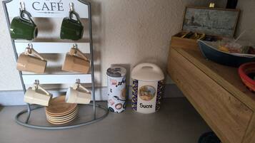 Een keukentafel met een koffiekop houder, een prullenbak en een houten kast.