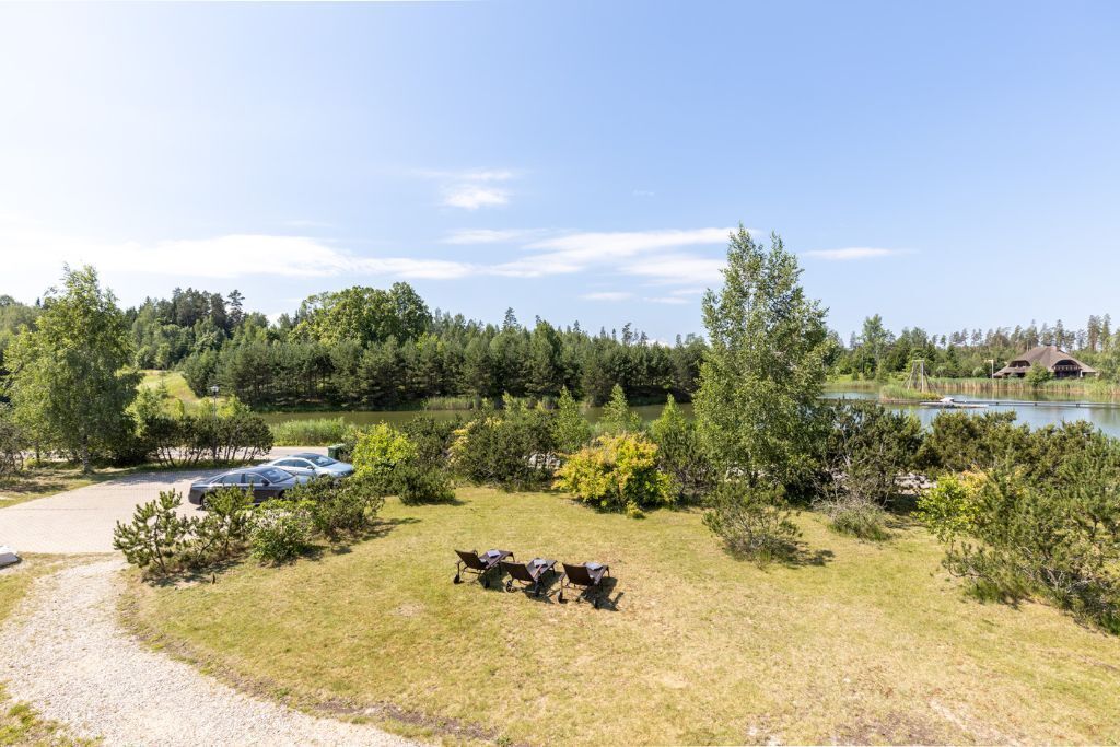 A grassy area with three camping chairs and a car parked near a lake, surrounded by trees and shrubs.
