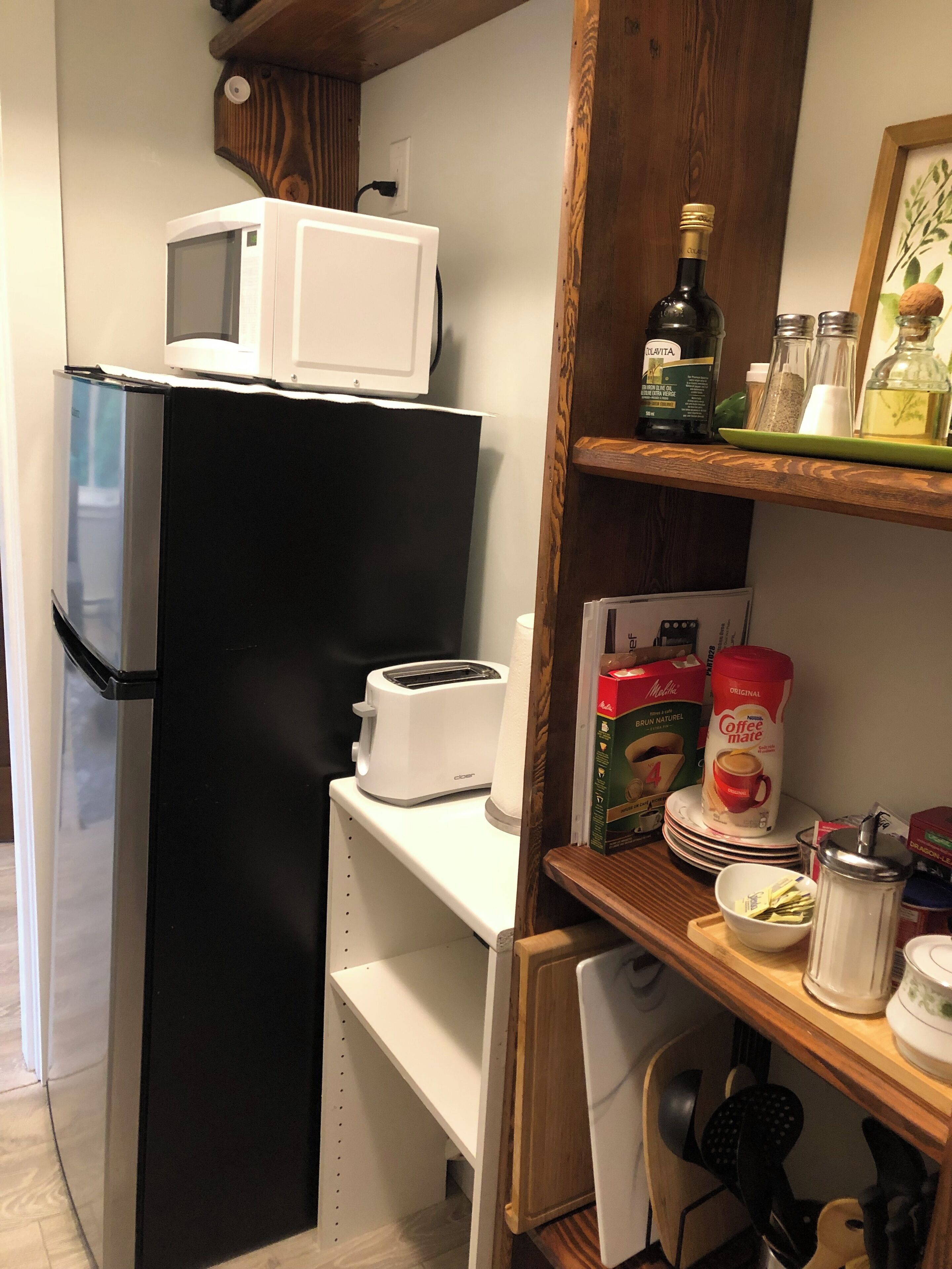 Una cocina compacta con un refrigerador negro, un microondas blanco, un tostador y una cafetera sobre una repisa.